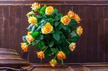 Potted bouquet of yellow roses placed on a wooden table against a dark wood-paneled background –...