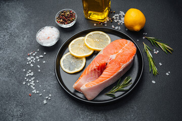 Fresh salmon fillet with lemon, herbs, and oil on a dark kitchen surface
