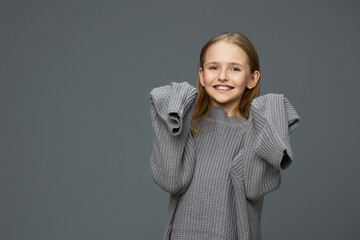 Smiling girl in a cozy gray sweater expressing joy against a minimalist gray background, showcasing emotion, comfort, and warmth in a seasonal, contemporary style