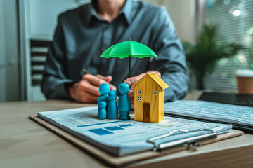 A wooden doll and wood house under an umbrella holding by agent represent insurance . house Family...