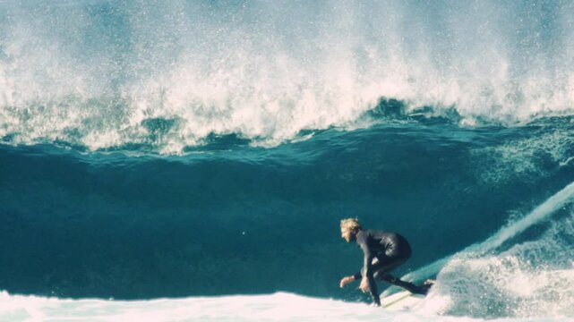 Blue wave breaks with surfer slotted in pocket as mist trails along curling back wall