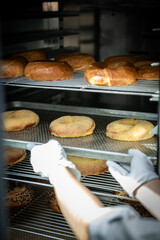 Baker putting fresh bagels in the oven at the bakery.