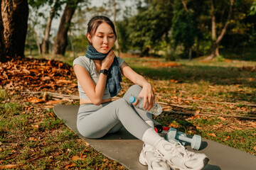 A woman dressed in workout clothes is holding a water bottle and wiping sweat from her face during...