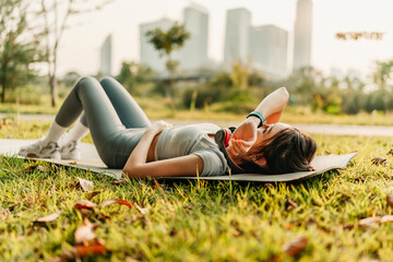 A woman dressed in workout clothes is holding a water bottle and wiping sweat from her face during...