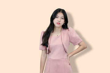 A young Asian woman in a pink dress and bolero smiles confidently at the camera, hand on hip,...