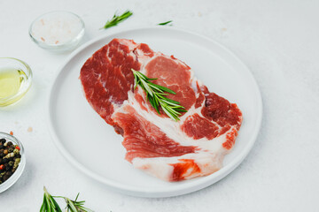 Uncooked pork steak on white plate with rosemary and pepper