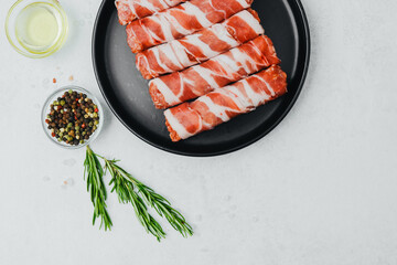 Bacon wrapped sausages on black plate with spices and rosemary