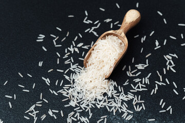 Wooden spoon filled with white rice grains on black surface