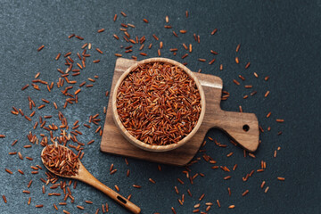 Red rice in wooden bowl on cutting board with scattered grains and spoon
