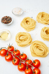 Raw tagliatelle pasta nests with tomatoes and spices on white background
