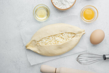 Raw khachapuri with egg yolk and cheese on white background with ingredients