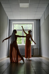 Silhouette of two dancers performing graceful artistic moves with their hands in corridor