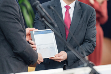 Speakers presenting a framed certificate at a media conference highlight. Their clear presentation...
