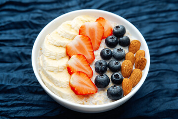 Oatmeal bowl with fruits and almonds on dark blue textile background
