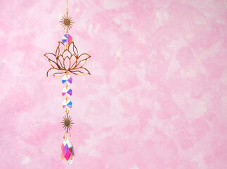 Hanging golden lotus ornament with crystal beads on pink background. Suncatcher.