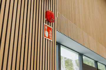 Naklejka premium Red fire alarm and fire emergency sign on a modern wooden slat wall inside a public building, close-up safety equipment