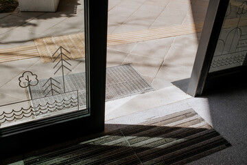 Entrance of a modern public building with tactile paving and safety mats, glass doors with...