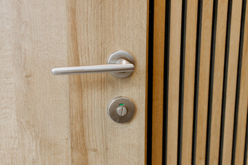 Close-up of a modern wooden door with stainless steel handle and occupied indicator lock in a...