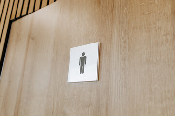 Modern wooden door with men's restroom symbol in public interior, minimal design for commercial...