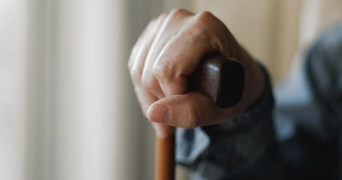 Hand of senior person holding knob of cane. Cropped close up shot elderly man suffering from skeletal system disorder, bones disease, health problems, recovering after trauma