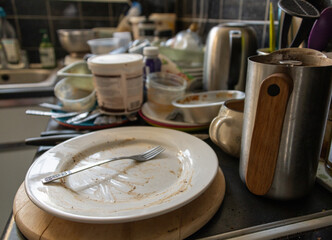 A messy and dirty kitchen worktop with unwashed plates, cutlery and recycling.