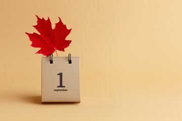 Minimal still life with a desk calendar showing "1 September" next to a red maple leaf. Symbolic image of back-to-school season and the start of autumn.

