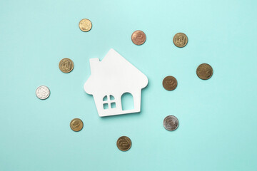 A white house model with scattered coins on a light blue background. Top view, flat lay.