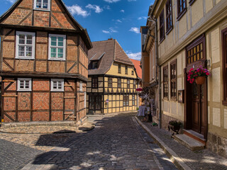 Charming half-timbered houses in Quedlinburg, Germany. Cobbled streets, medieval architecture, and traditional signage like “Quedlinburger Senf” highlight this UNESCO World Heritage Site.