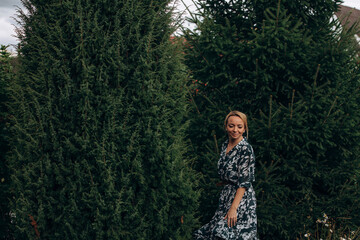A young adult woman walks in the park among the fir trees