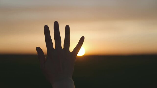 Reaching out to the sun, happy girl at sunset, sunlight shining on her hand, solar system star, happy family concept, touching a dream, asking for help from God, natural phenomenon.