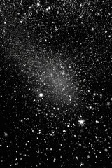 A grayscale astrophotograph reveals a diffuse, elongated comet against a backdrop of countless stars, varying in brightness and size, scattered across the dark expanse of space