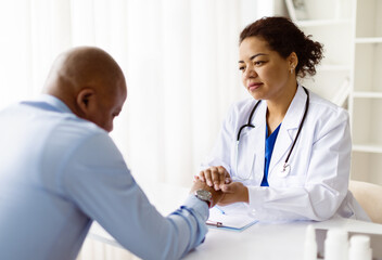 Thoughtful african american female doctor holding hands of male patient during emotional...