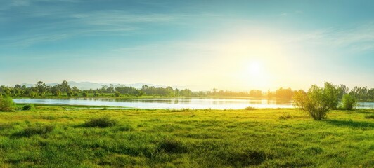 Obraz premium The tranquil river landscape at sunrise with lush green grass and trees.