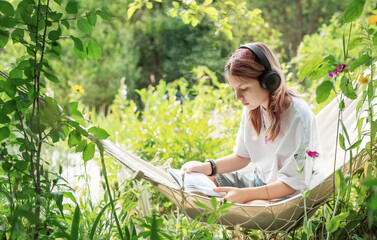 Teenage girl reading and listening to music in hammock in garden