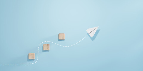 Paper plane flying over wooden blocks with curved dashed line on soft blue background. Concept of business strategy, creative thinking, success path, and goal achievement.