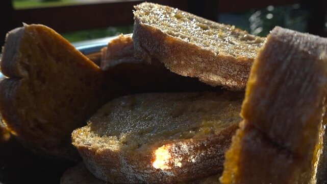 Gorgeous close up or closeup footage of hand adding oiled and golden ciabatta bread slices into a metal shiny bowl during a sunny summer day, preparing the bread for grilling or cooking, delicious.