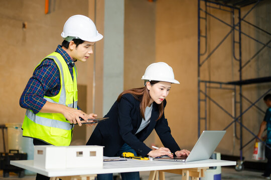 Construction professionals in hard hats examine blueprints and a scale model on a worktable, collaborating on building design