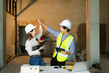 Two construction professionals in hard hats and safety vests raise their fists in celebration over...
