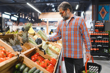 Stylish senior man in red shirt choosing vegetables and fruits at supermarket