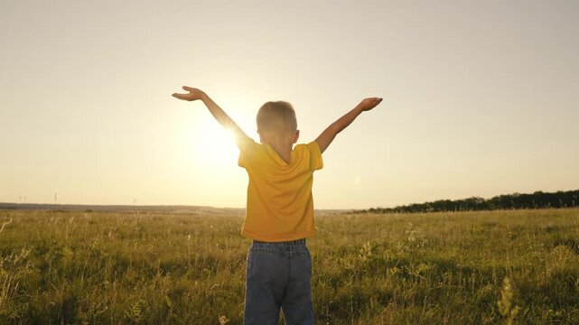 little child with hands raised up at sunset, boy believes in religion in the rays sunlight in the sky, happy family, kid son looks into the distance dawn, boy's summer sunny day, adventure travel fun.