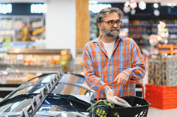 Bearded man with frozen fish his hands stands at the refrigerator in the department of frozen food