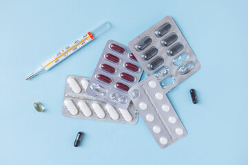 Classic mercury thermometer and white round tablets on a blue background. Healthcare and flu...