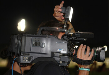 Camarógrafo audiovisual de noche con cámara de vídeo filmando con flash de iluminación auxiliar...