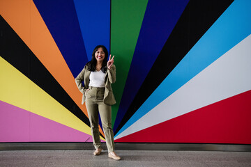 Businesswoman in a suit standing in front of a vibrant colorful wall making peace sign