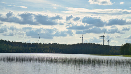 Lake with reflective surface, wind turbines in the background, cloudy sky.