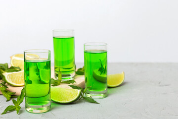 Sweet refreshing mint liqueur, with ice and mint leaves on table background, Shots with lime slice and mint flat lay