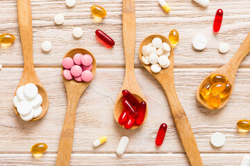 Vitamin capsules in a spoon on a colored background. Pills served as a healthy meal. Red soft gel...