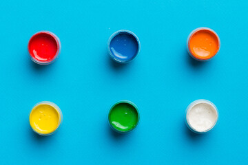 jars with gouache of different colors on Colored background. hobby painting. Top view with empty...