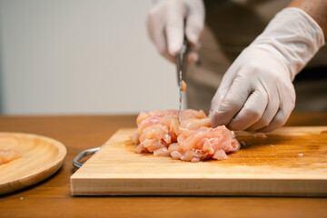 Asian man's hands cutting meat on a wooden cutting board in the kitchen, preparing to cook.