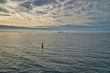 Green buoy in the calm sea at sunrise, ships on the horizon and dramatic sky